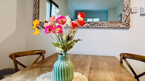 Ein Holztisch mit einer grünen, gestreiften Vase voller Blumen auf einer weißen Tischdecke.