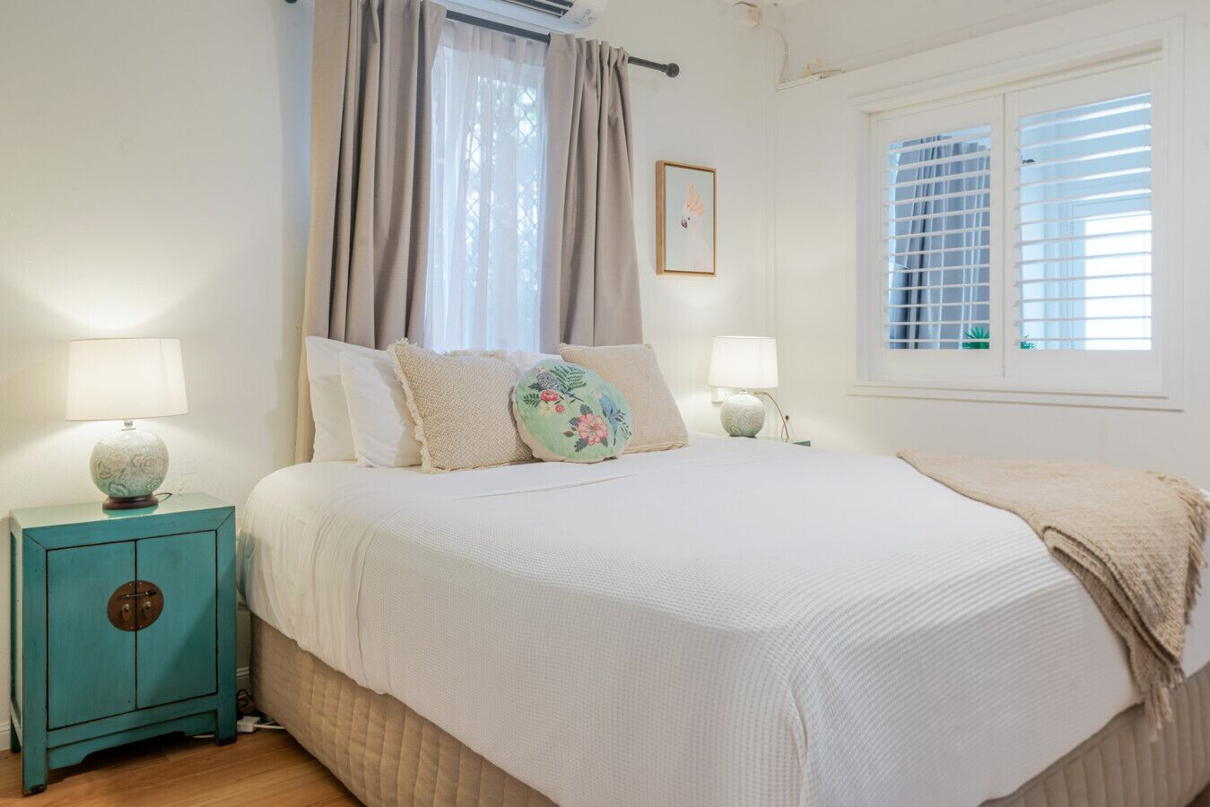Ein Schlafzimmer mit einem Bett, zwei Nachttischen, einem Fenster mit Jalousien und einer Wand-Klimaanlage.