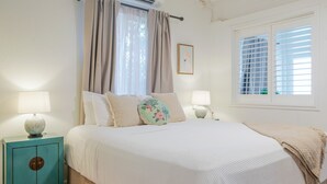 Ein Schlafzimmer mit einem Bett, zwei Nachttischen, einem Fenster mit Jalousien und einer Wand-Klimaanlage.