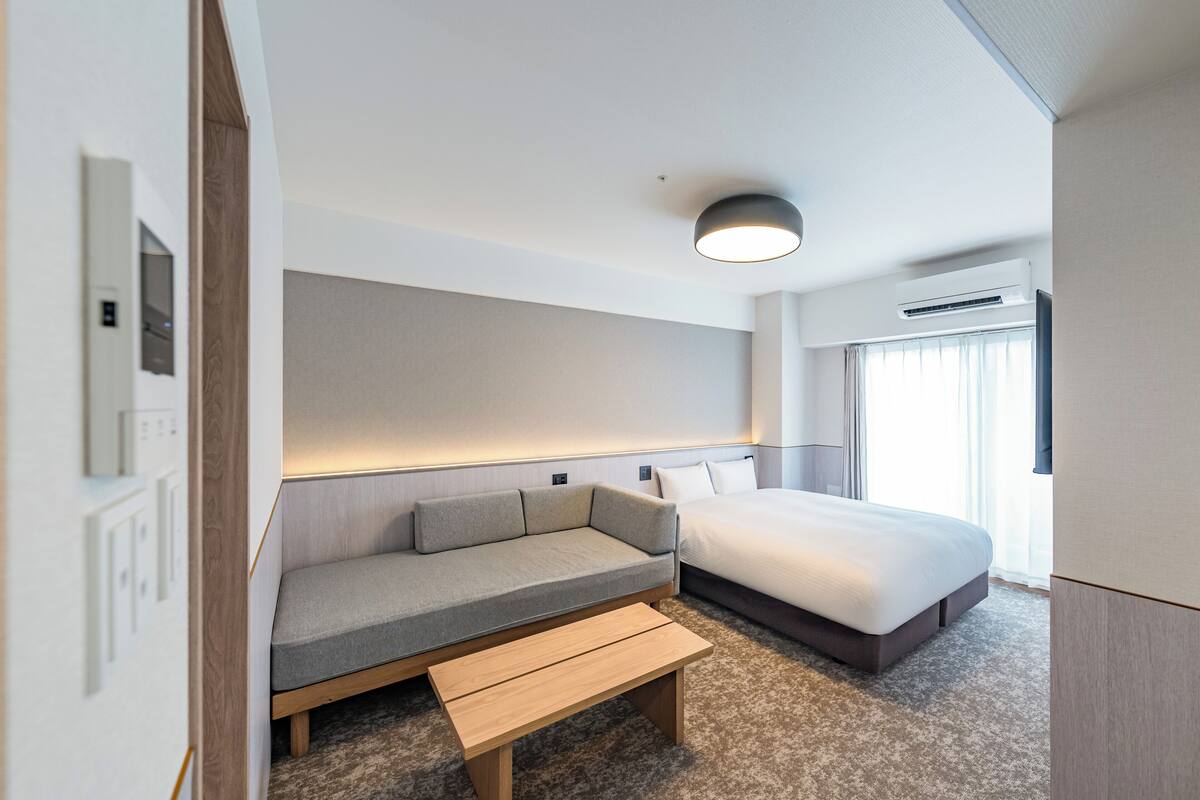 Une chambre d’hôtel moderne équipée d’un lit, d’un canapé, d’une petite table et d’un luminaire au plafond.