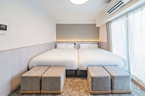 A hotel room with a double bed, two bedside tables, a wall-mounted air conditioner, and a large window with curtains.