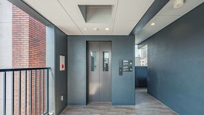 A hallway with a modern design, featuring a metal railing, a door with a glass panel, and a sign on the wall. - Apartment Hotel 11 Dotonbori 7 (Osaka)