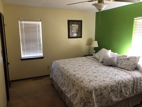 A bedroom with a bed, a nightstand, a lamp, a framed picture, and a window with blinds.