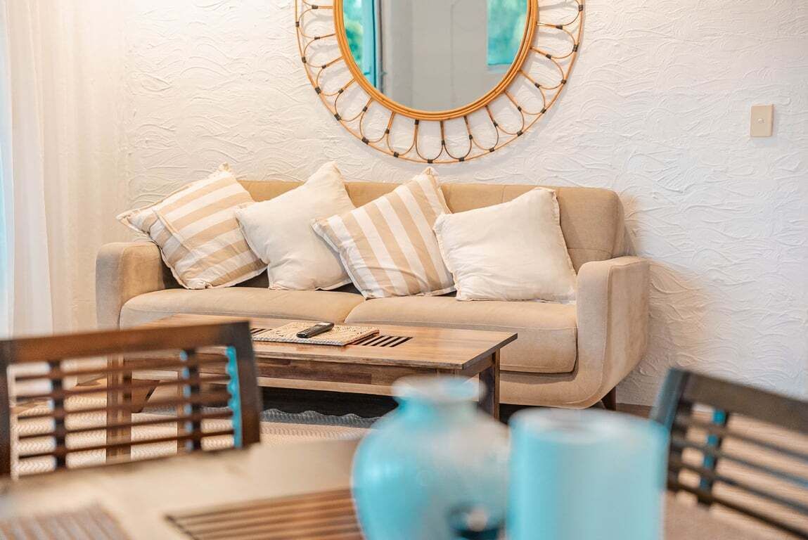 A living room with a beige sofa, striped pillows, a round mirror, and a wooden coffee table.