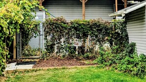 A two-story house with a covered patio, a garage, and a garden with a hedge and plants. - Waterfront Comfy Guesthouse, Prince Edward County (Carrying Place)