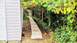 A pathway leading to a white building with a 'Guest Entrance' sign, surrounded by lush greenery and vines. - Waterfront Comfy Guesthouse, Prince Edward County (Carrying Place)