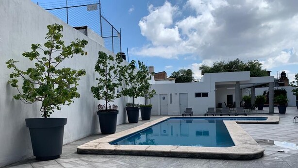 A swimming pool area with tiled flooring, potted plants, and a white building in the background.