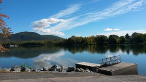 A calm lake with a dock and rocky shoreline, surrounded by trees and a mountain in the background. - Bright 2BR Near River · Private Parking (McMasterville)