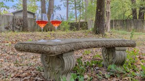 Un banc en pierre sur lequel reposent deux verres à vin, entouré d’arbres et d’une clôture en bois.