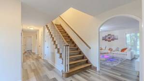 Un intérieur moderne avec un escalier en bois, un ensemble de canapés blancs et un tapis à motifs.