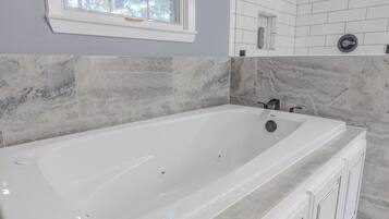 A modern bathroom with a large white bathtub, marble tiles, and a window.