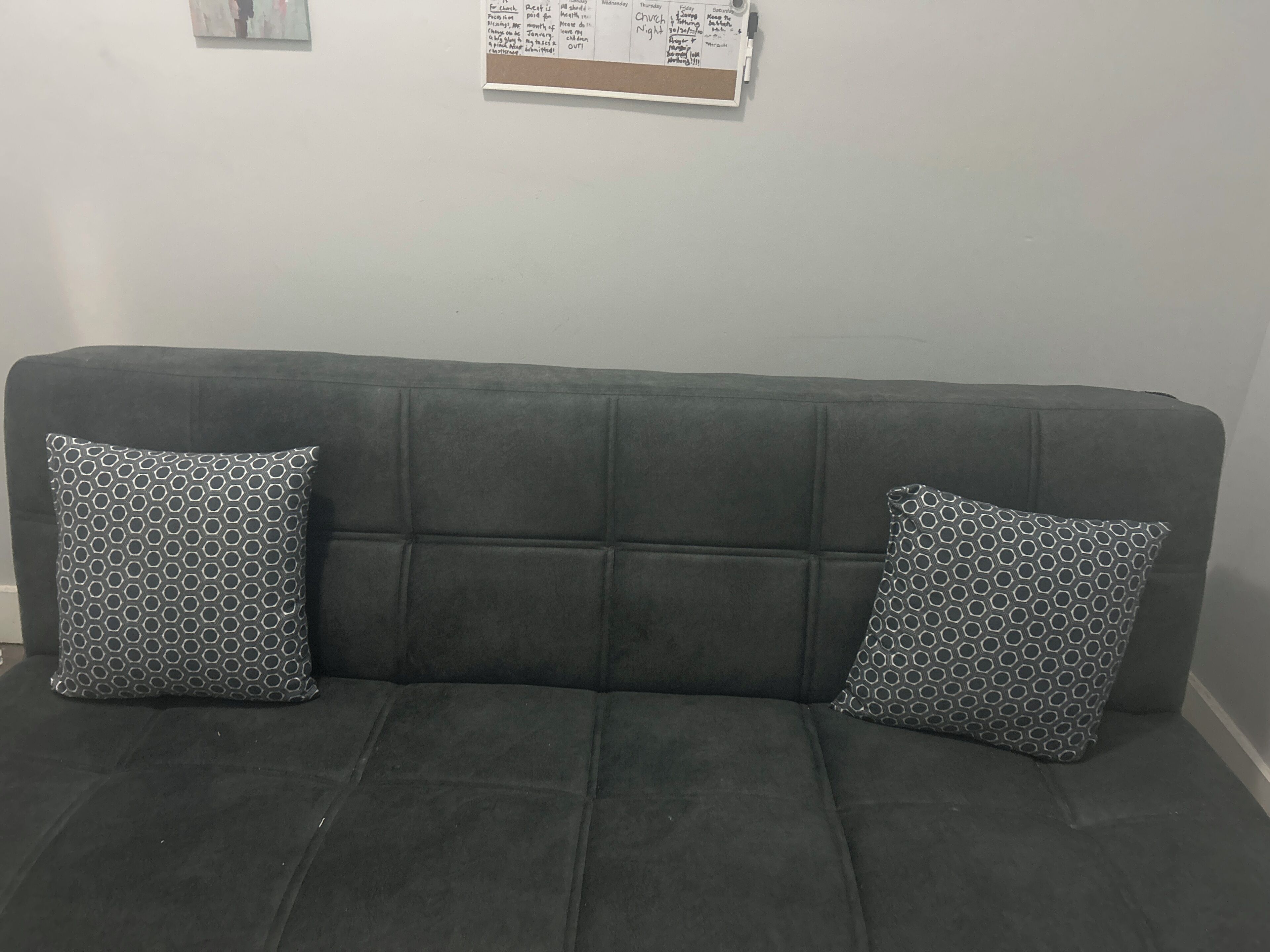 Un sofá gris con dos cojines estampados y un tablón de anuncios en la pared de fondo.