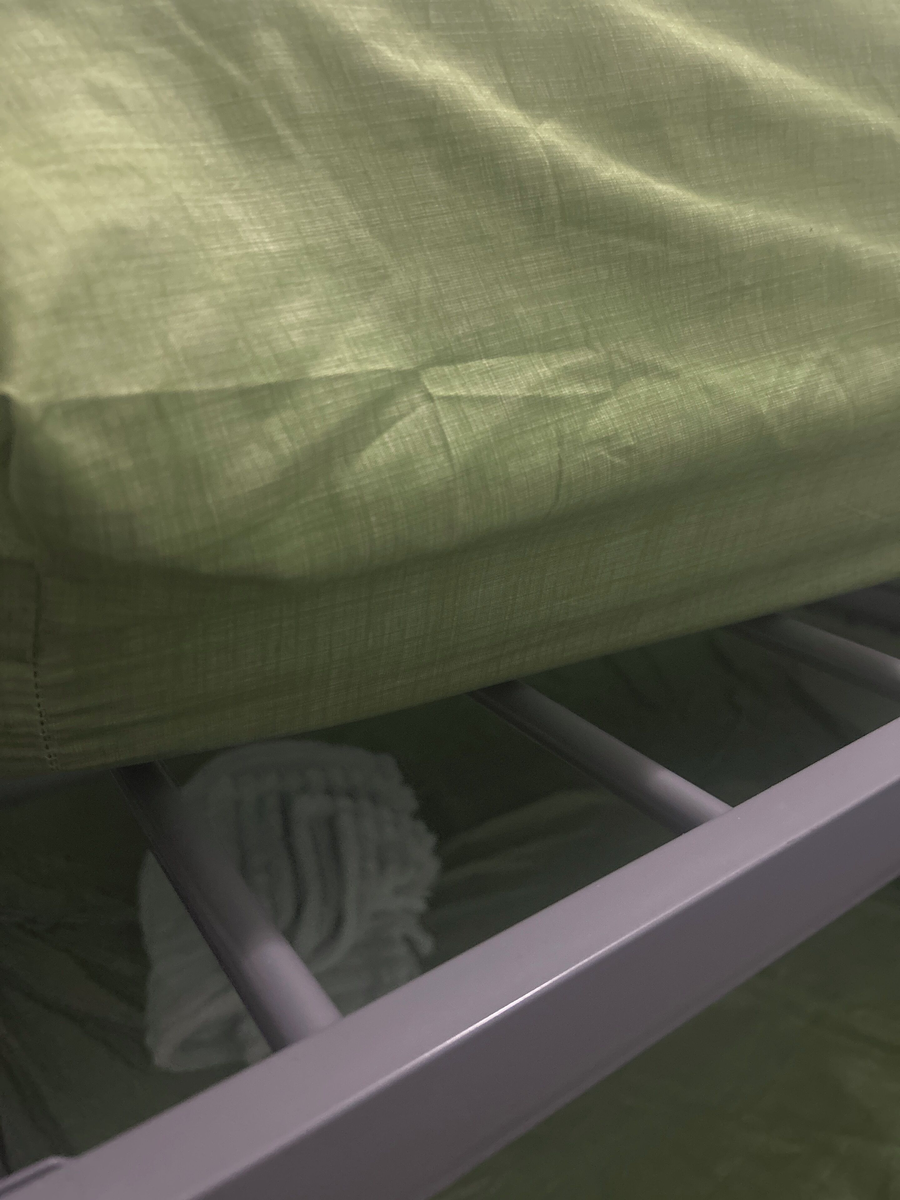 Ein Bett mit einer grünen Decke und einem weißen Kopfkissen.