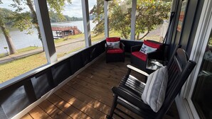 A covered porch with wooden flooring, two wicker chairs with red cushions, and a bench. - Waterfront Paddles & Pours Cottage on Claytor Lake (Hiwassee)