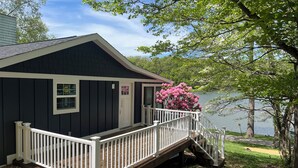 A dark wooden cabin with a white porch and a small staircase leading to a deck. - Waterfront Paddles & Pours Cottage on Claytor Lake (Hiwassee)