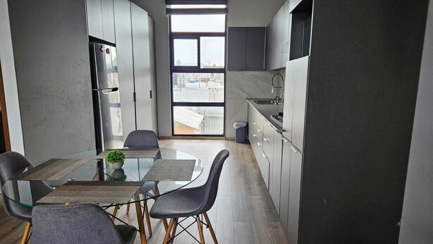 A modern kitchen with a dining area, featuring a glass table, grey chairs, and a view through large windows. - Mia La Perla Apartment, very close to La Perla District, Plaza del Sol, Expo GDL (Zapopan)