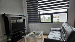 A living room with a flat-screen TV, a glass coffee table, a leather sofa, and a window with blinds. - Mia La Perla Apartment, very close to La Perla District, Plaza del Sol, Expo GDL (Zapopan)