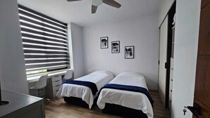 A bedroom with two beds, a desk, and a ceiling fan. - Mia La Perla Apartment, very close to La Perla District, Plaza del Sol, Expo GDL (Zapopan)