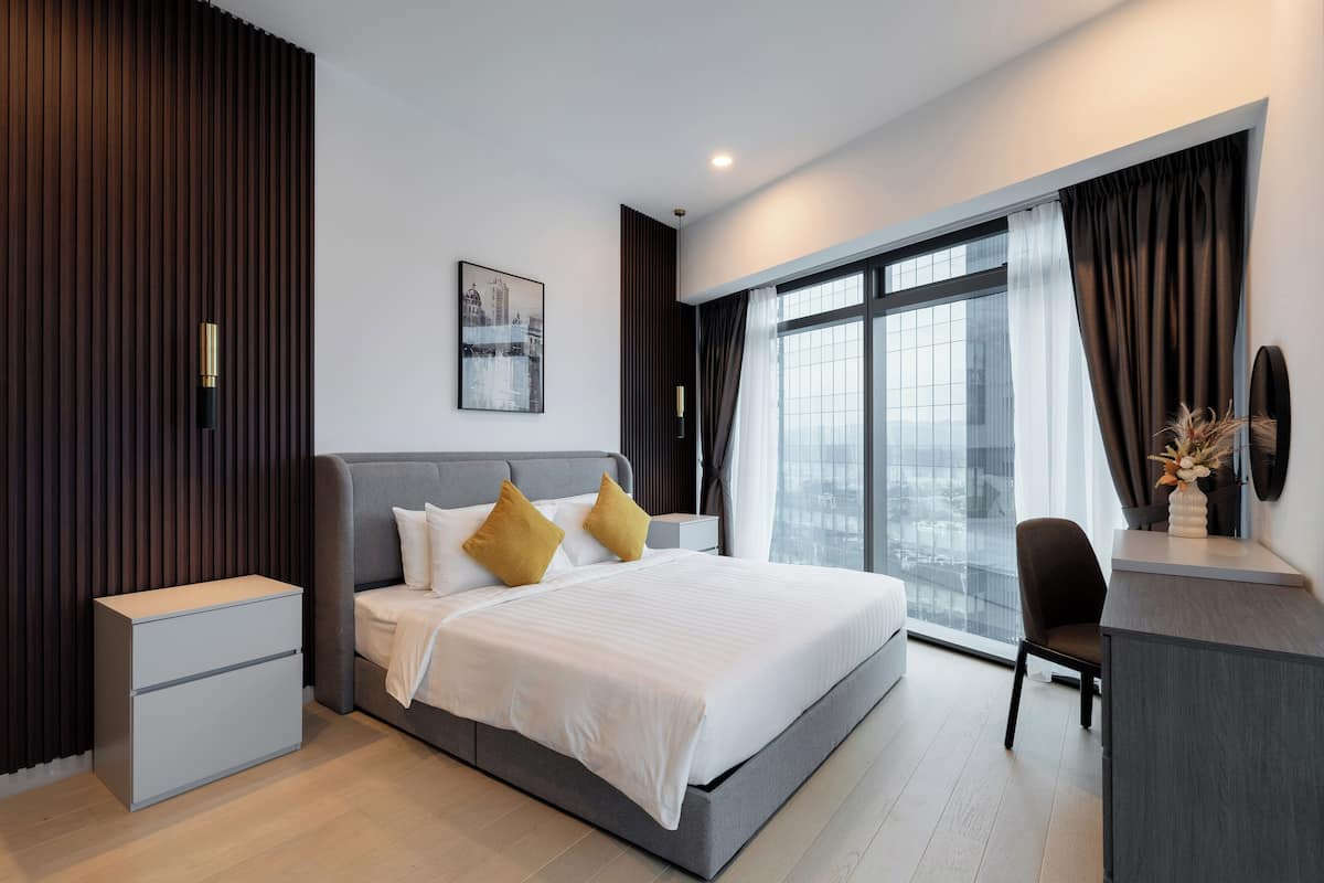 Un dormitorio moderno con una cama grande, mesitas de noche, un escritorio y vistas de la ciudad a través de amplios ventanales.