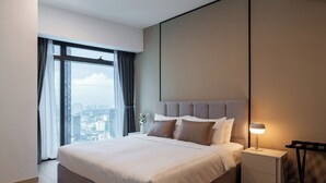 A modern hotel room with a large bed, a nightstand with a lamp, and a view of the city through a large window.
