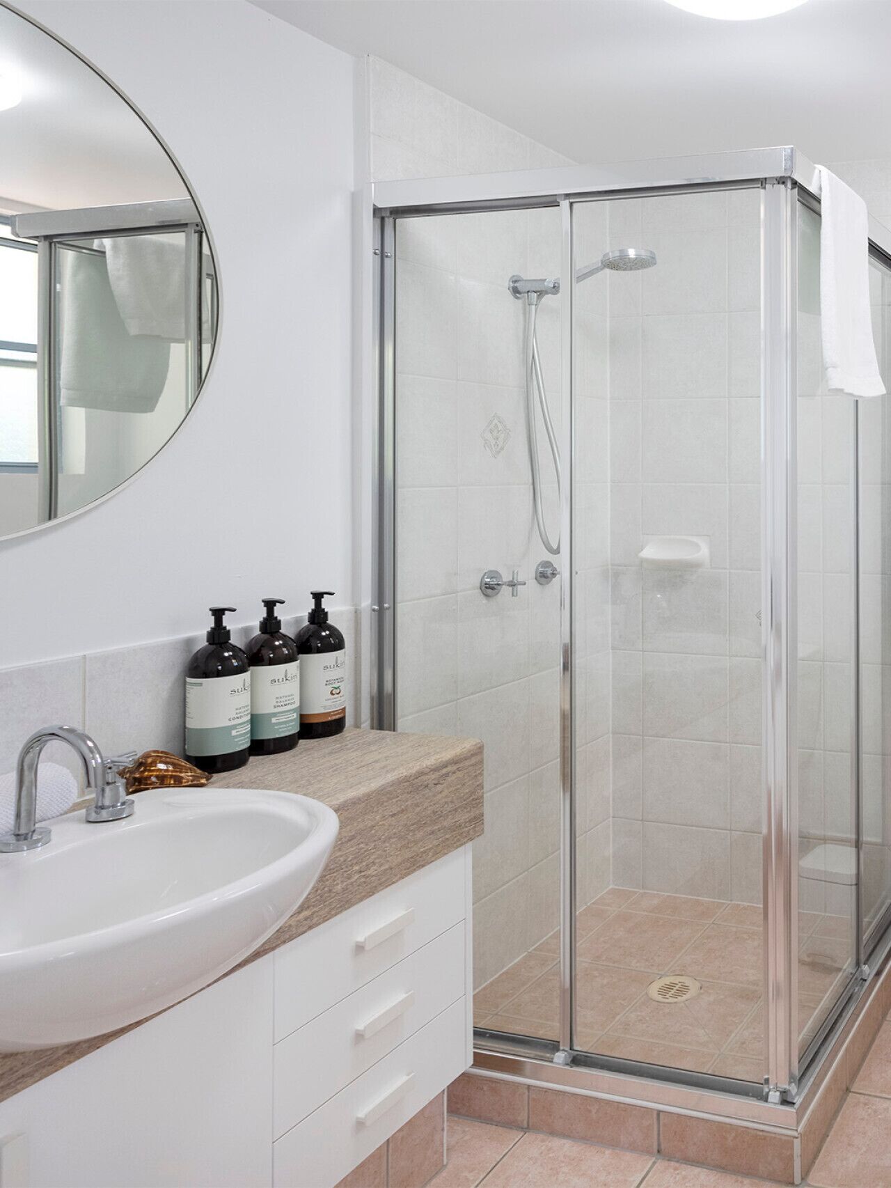 A modern bathroom with a glass-enclosed shower, a white sink, and a large mirror.