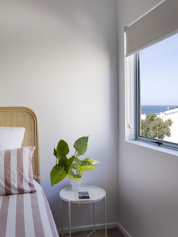 A bedroom with a bed, a small round table with a plant, and a window with a view of the sea.