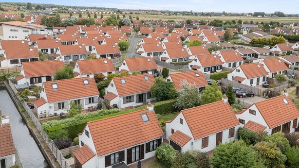 Een woonwijk met gelijkmatige huizen, herkenbaar aan rode dakpannen en witte muren, die in rijen langs een smalle straat staan.