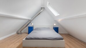 Een moderne, minimalistische slaapkamer met een schuine kap, dakraam en een centraal geplaatst bed.