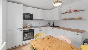 Een moderne keuken met witte kasten, een houten aanrecht, een ingebouwde oven, een koffiezetapparaat en een gele hanglamp.