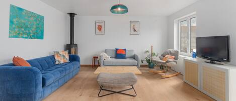 A modern living room with a blue sofa, a grey armchair, a wooden coffee table, and a television on a cabinet.