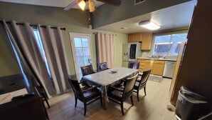 Uma área de refeições com uma mesa, cadeiras, um ventilador de teto e vista para a cozinha.