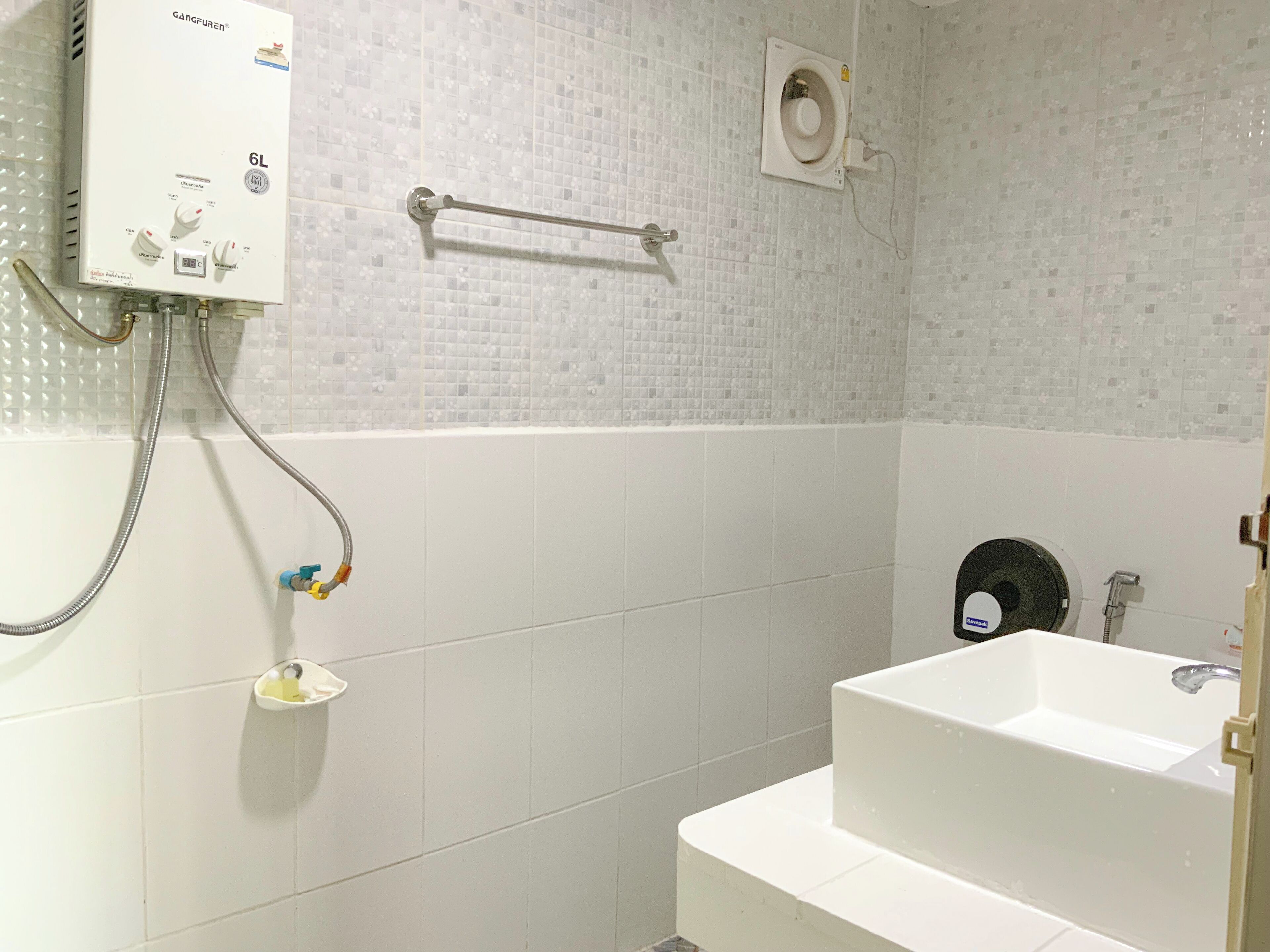 Ett badrum med ett vitt badkar, en dusch och en toalett. Ovanför duschen finns en handduksställning och på väggen sitter en hållare för toalettpapper.