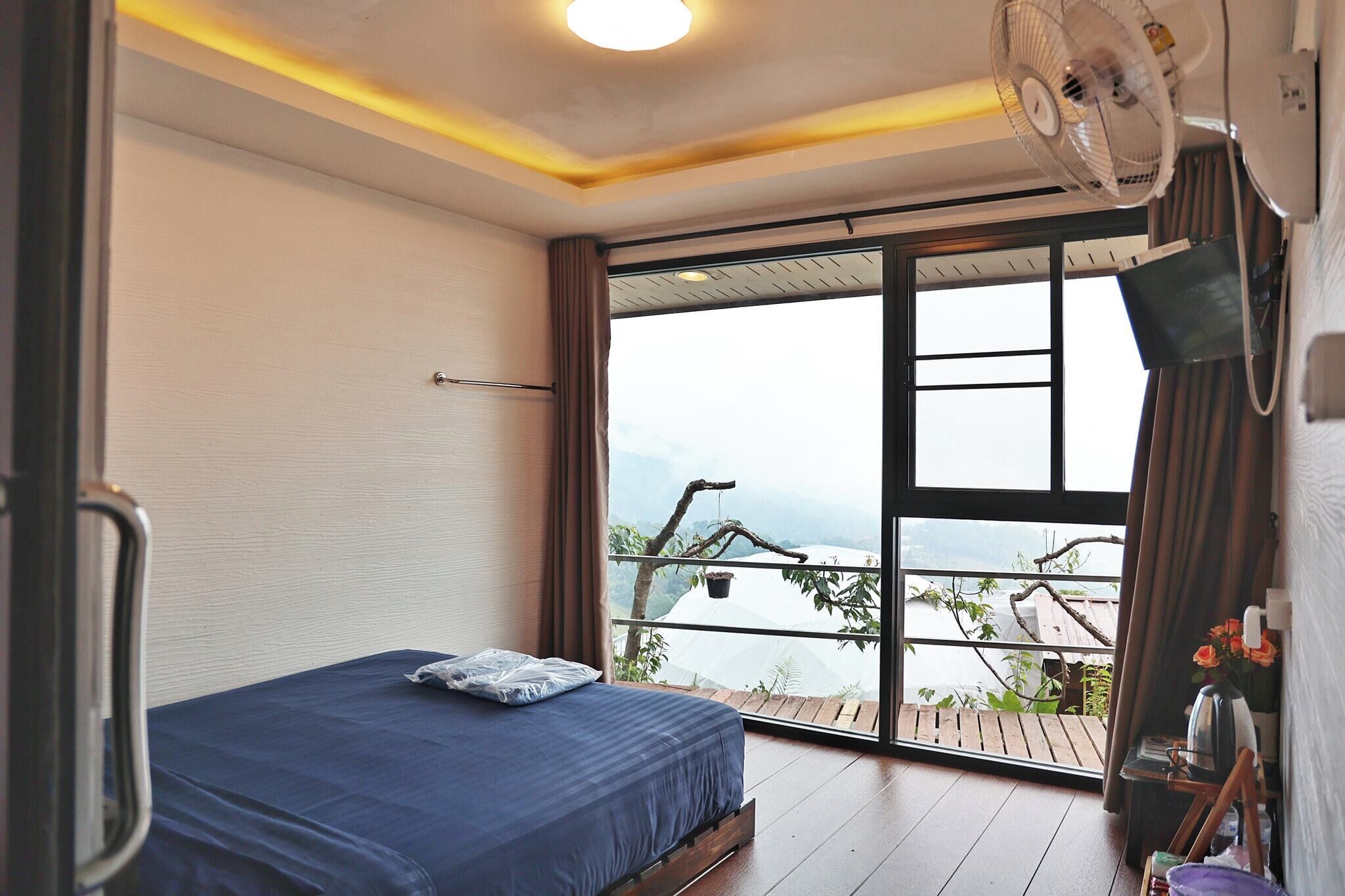 Un dormitorio con cama, ventilador, televisión y vista a un balcón con un árbol.