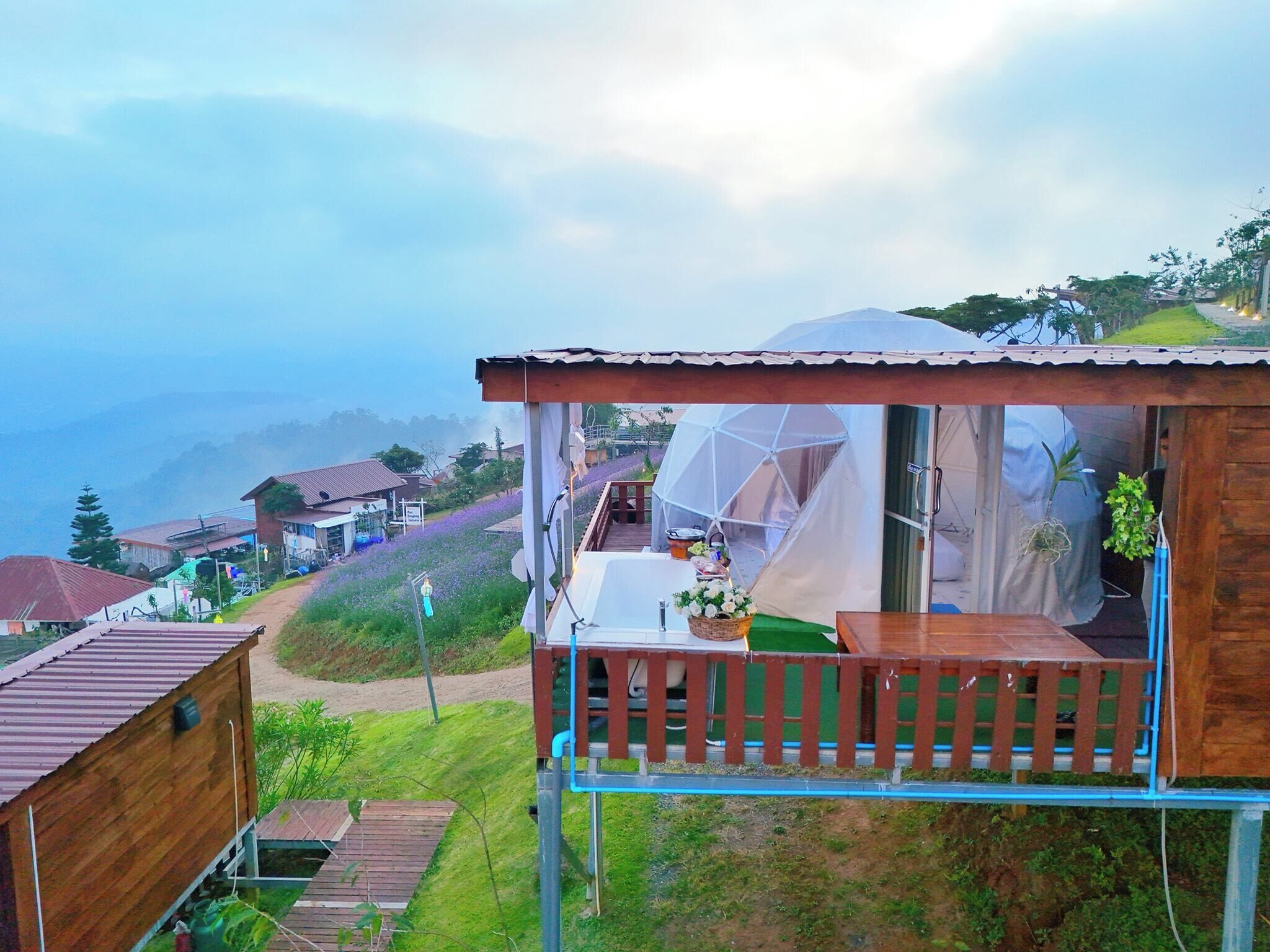A wooden cabin with a balcony, a transparent dome structure, and a view of a hillside with houses.