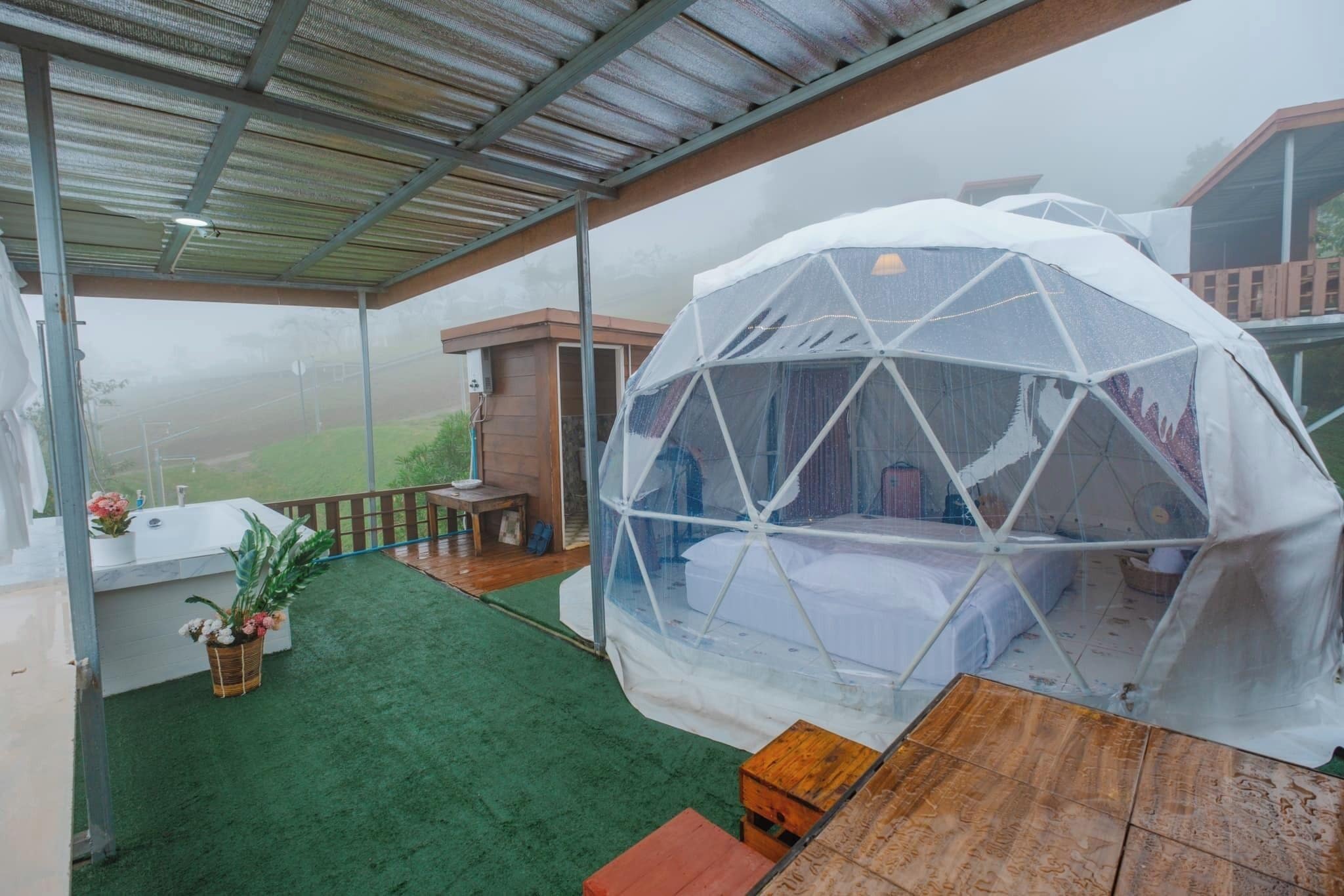 A transparent dome structure with a wooden table and bench, surrounded by a green artificial lawn and a wooden deck.