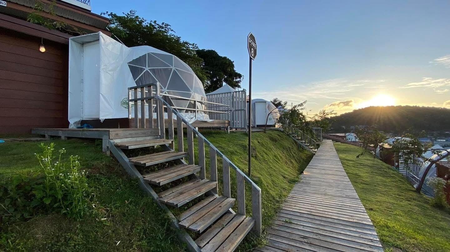 A wooden staircase leading to a white dome structure, a wooden pathway, and a sunset in the background.