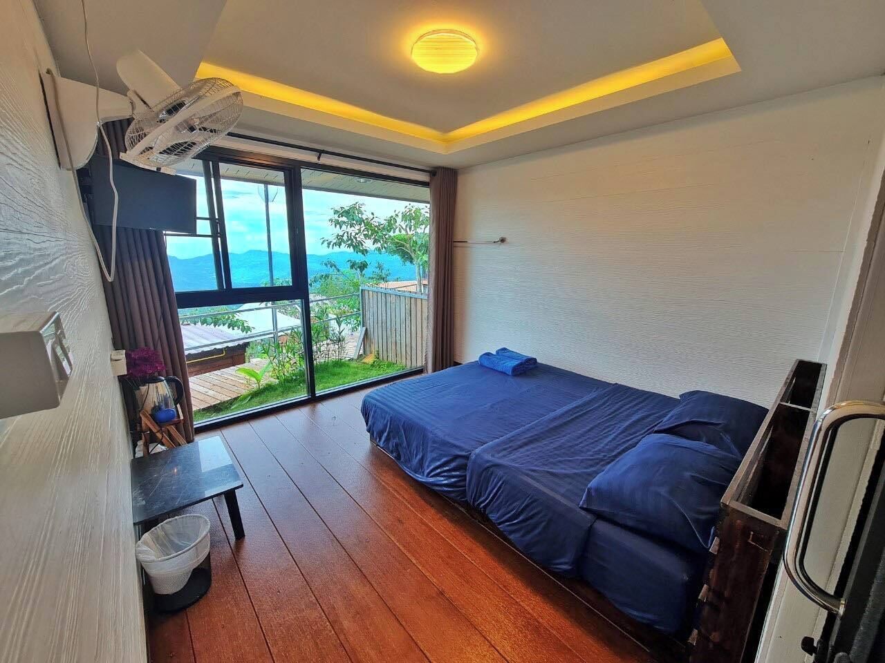 Un dormitorio con cama, una mesita, una silla y ventana con vistas a zonas verdes y montañas.