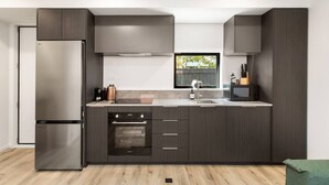 Une cuisine moderne avec des meubles de couleur sombre, des appareils en acier inoxydable, une fenêtre et une vue sur la verdure à l’extérieur.