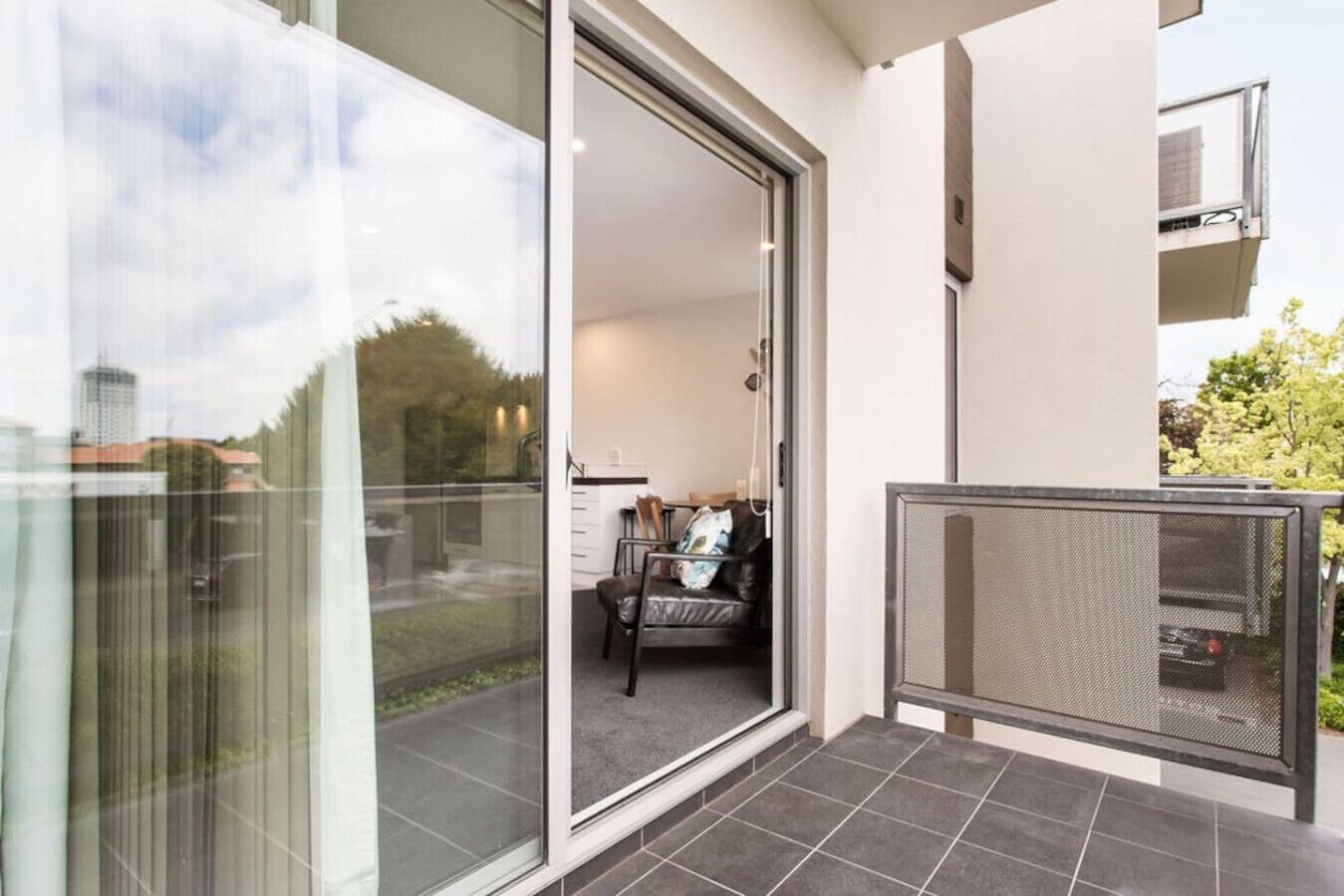 Eine moderne Wohnung mit einer Schiebetür, die auf einen Balkon führt, einer kleinen Sitzecke mit Sofa und Tisch sowie Blick auf die Umgebung.
