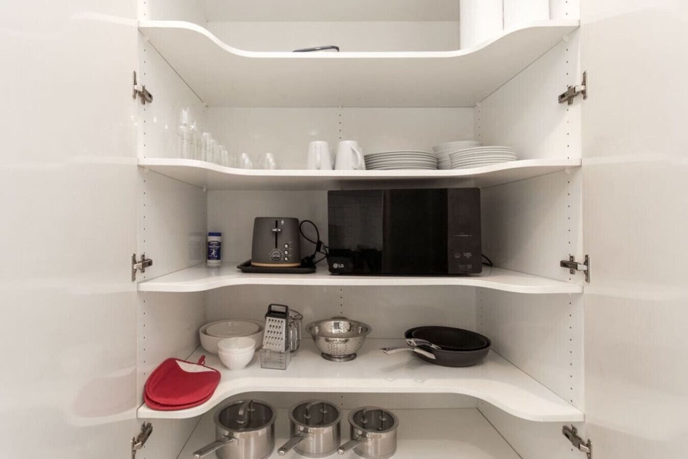 Una cocina con armarios blancos, microondas, cafetera, rallador y ollas.