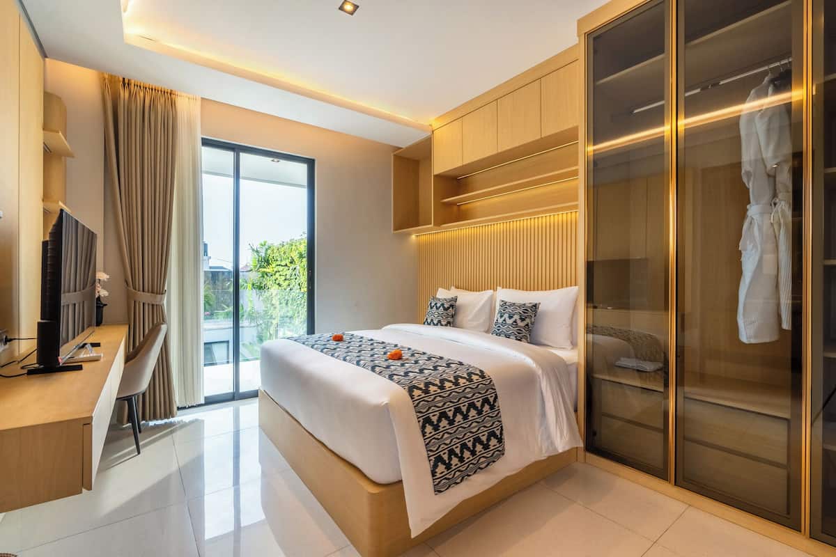 Una habitación de hotel moderna con una cama grande, un escritorio con ordenador, un armario y un ventanal corredero al exterior.