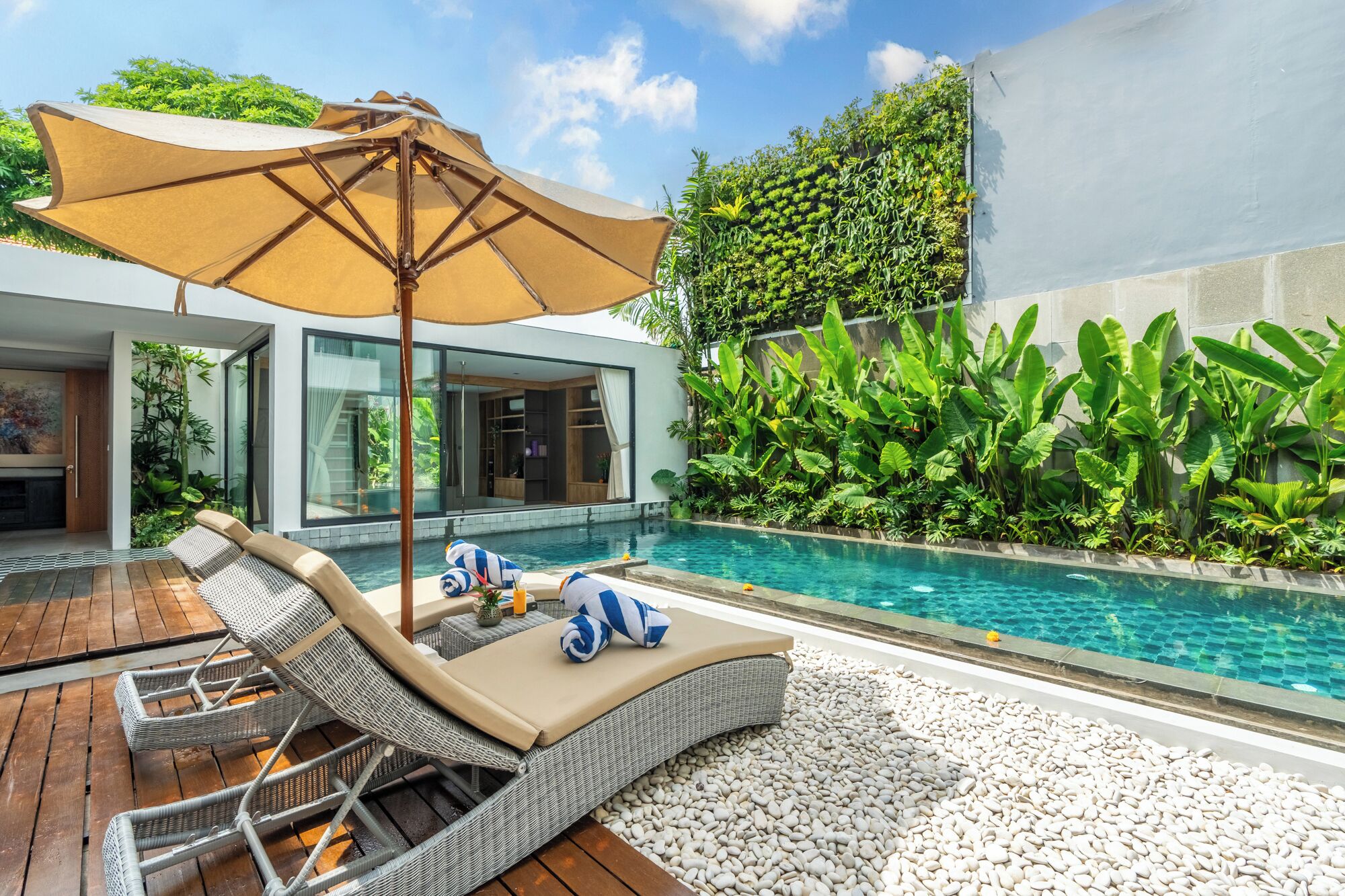 Un espace piscine extérieur moderne, doté de chaises longues, d’un grand parasol et d’une végétation luxuriante.