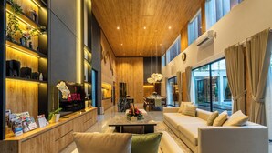 Un moderno vestíbulo de hotel con un mostrador de recepción de madera, una zona de estar con sofás, una mesa de comedor y un amplio ventanal con vistas al exterior.