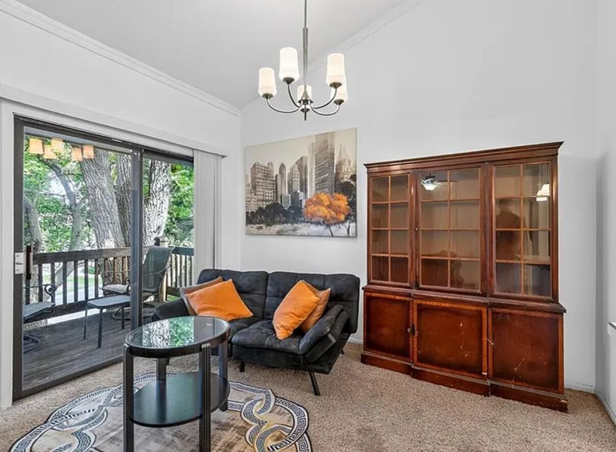 Un salon avec un canapé en cuir noir, une table basse en verre, un tapis à motifs, un meuble en bois et un tableau représentant un paysage urbain accroché au mur.