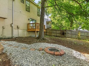 A backyard with a tree, a fire pit, and a wooden deck.