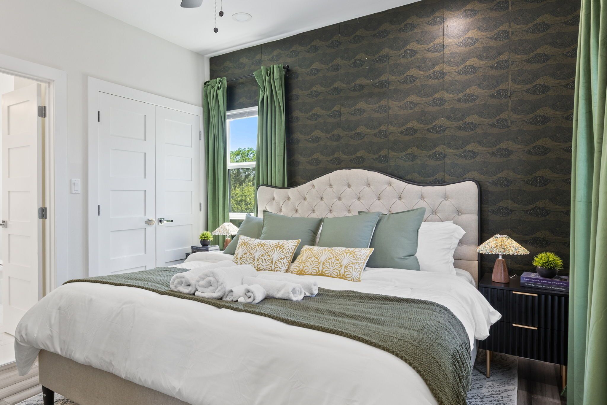 A neatly made bed with a tufted headboard, green and white bedding, and a set of towels.