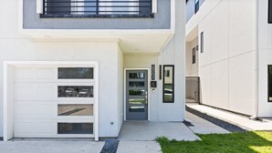 A modern two-story building with a white facade, a garage with multiple doors, and a small front yard with grass and gravel.