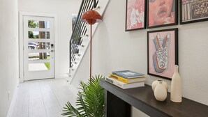 A modern hallway with a staircase, a floor lamp, framed artwork, and a small table with books and vases.