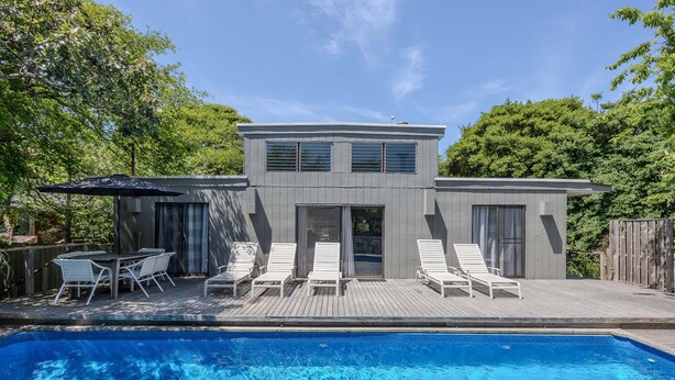 Una casa moderna de dos pisos con piscina, un deck con sillones de descanso y una cerca de madera.