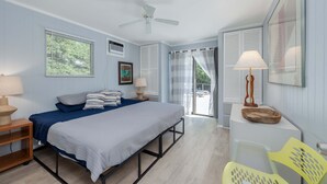 Un dormitorio con cama, mesitas de noche, ventilador de techo y vistas al exterior.